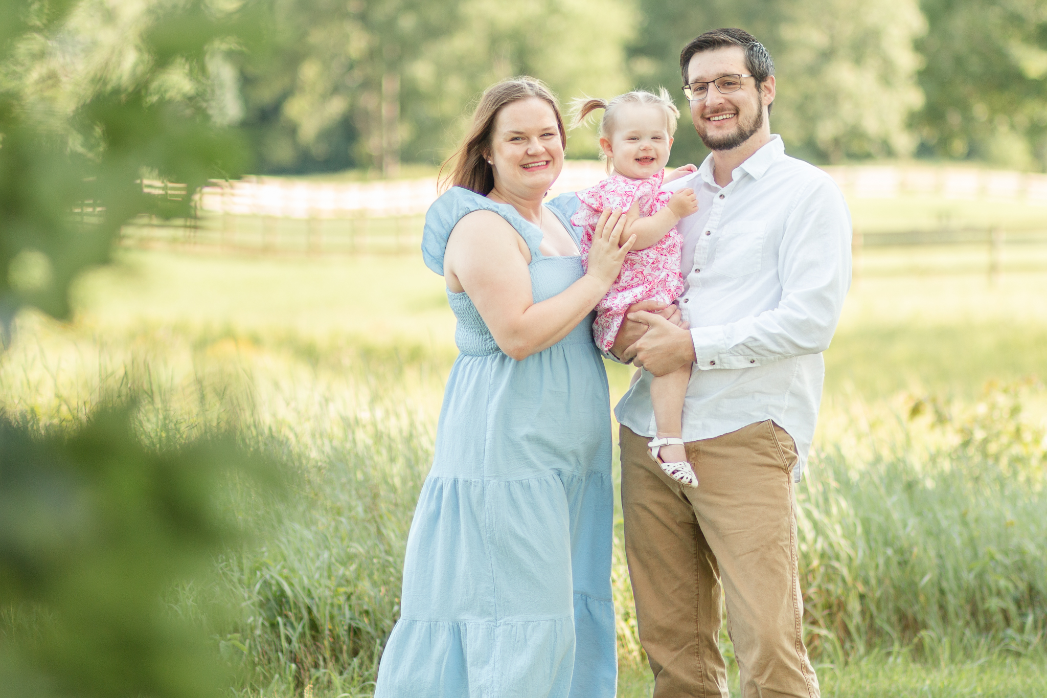 Mom, dad and daughter pose for a family photo outside at golden hour